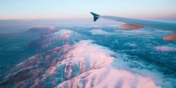 view from a plane, overlooking the wing, and mountain peaks with snow