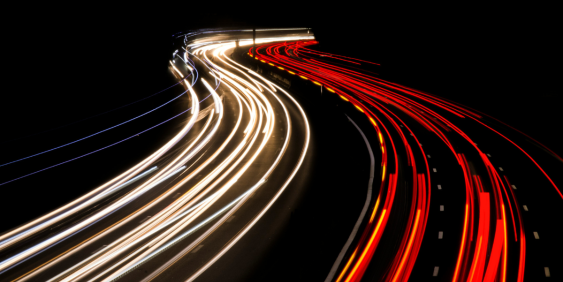  Long exposure photo of a highway at night, showcasing light trails from moving vehicles against a dark sky.
