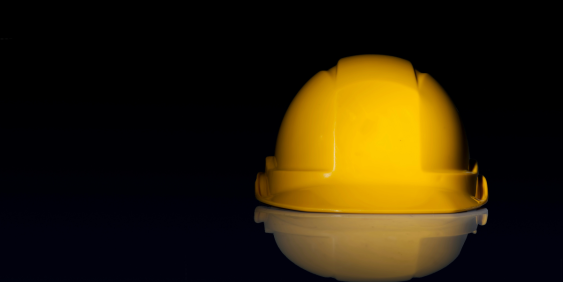 A yellow hard hat resting on a shiny reflective surface, showcasing its bright color and smooth texture.