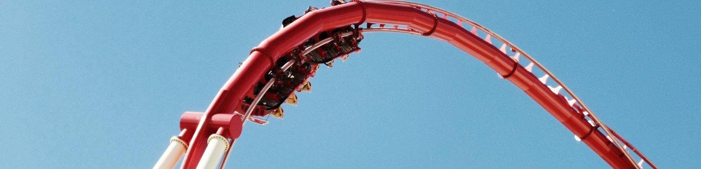Red roller coaster ascending a steep curve against a clear blue sky, conveying excitement and thrill.