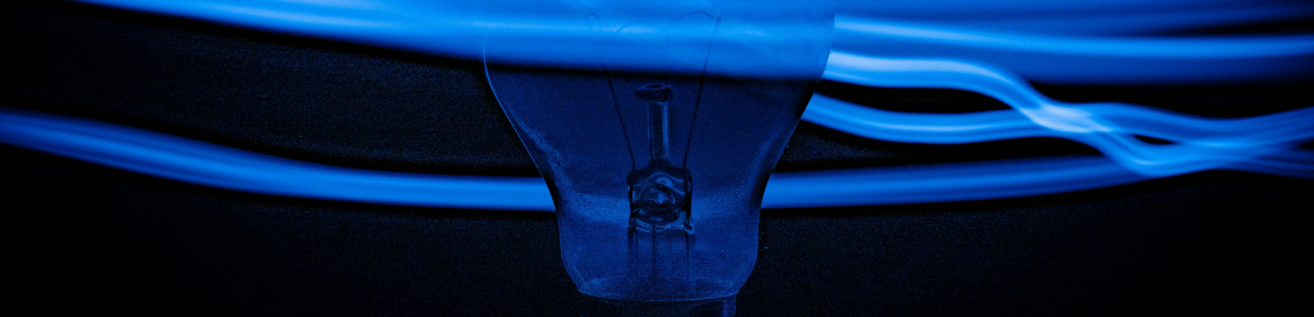 A dark, silhouetted light bulb is surrounded by dynamic, swirling blue light trails against a black background, creating a sense of energy and motion.