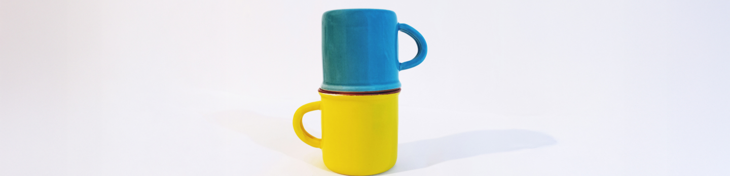 Two stacked mugs on a white background; a blue mug sits inverted on top of a yellow mug.