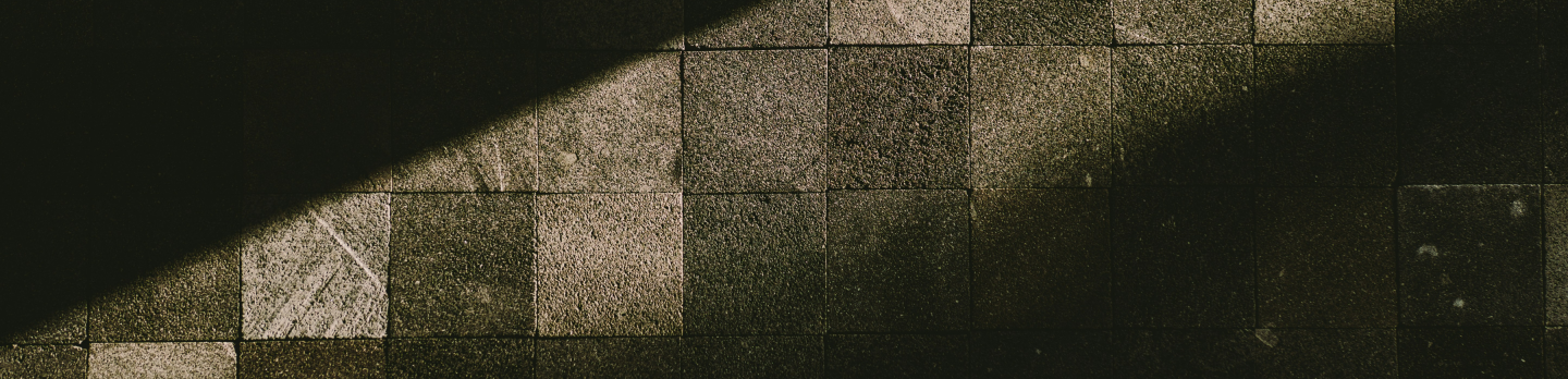 Dimly lit stone tiles with a diagonal shadow create a geometric pattern. The textured surface and subtle light evoke a calm, moody atmosphere.