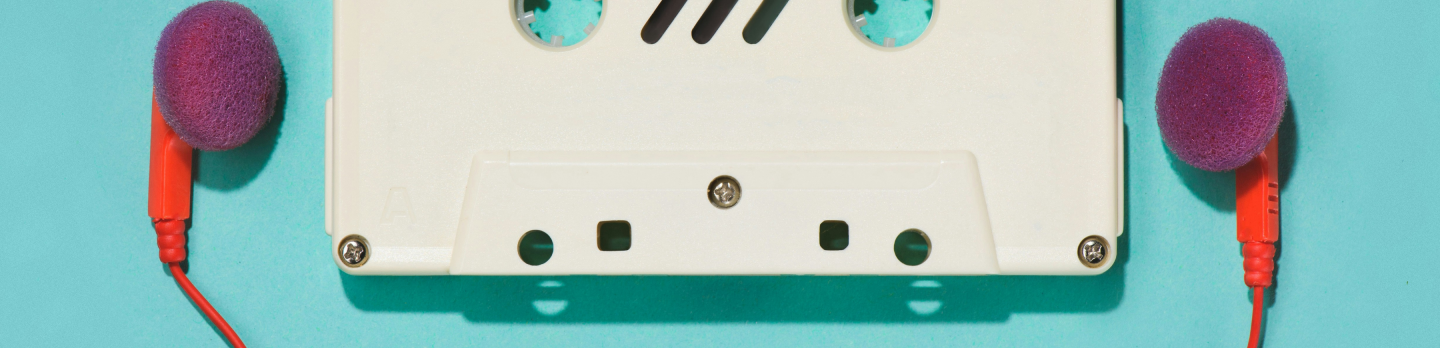 A white cassette tape lies flat on a blue background, flanked by two purple foam-covered earbuds with red cords, conveying a retro, nostalgic vibe.