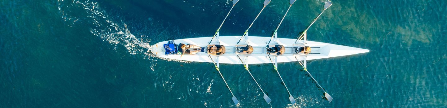 Aerial view of a sailboat gliding across the deep blue ocean, surrounded by gentle waves and sunlight reflections.