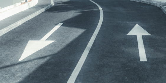 A road with two arrows indicating opposite directions, symbolizing diverging paths or choices ahead.