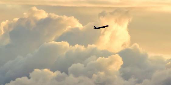 A plane soaring through fluffy white clouds against a bright blue sky.