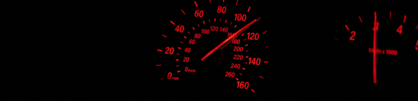 A red speedometer illuminated in the dark, displaying high speed with a glowing needle pointing towards the maximum limit.