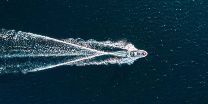 Overhead perspective of a boat moving across the vast ocean, leaving a wake in the water.
