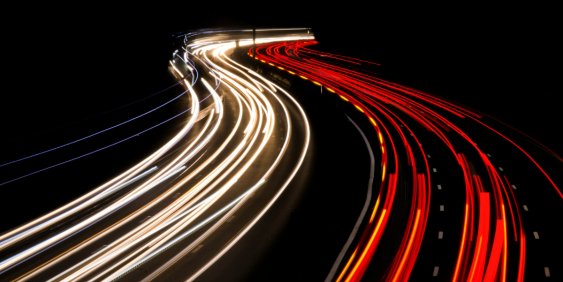  Long exposure photo of a highway at night, showcasing light trails from moving vehicles against a dark sky.