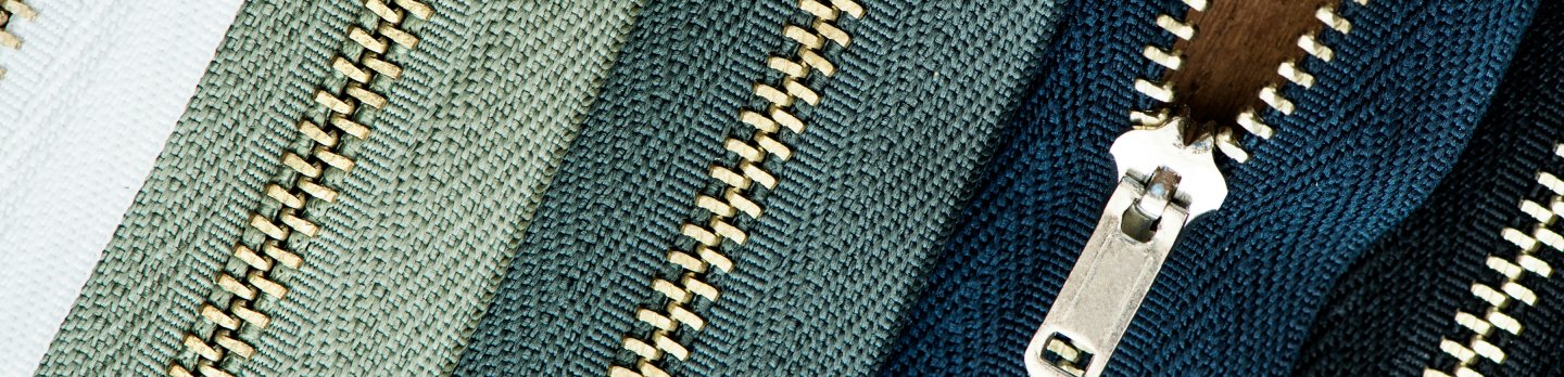 Close-up of colorful zippers arranged in parallel. Fabrics are white, green, and blue, with metallic teeth. The tone is vibrant and orderly.