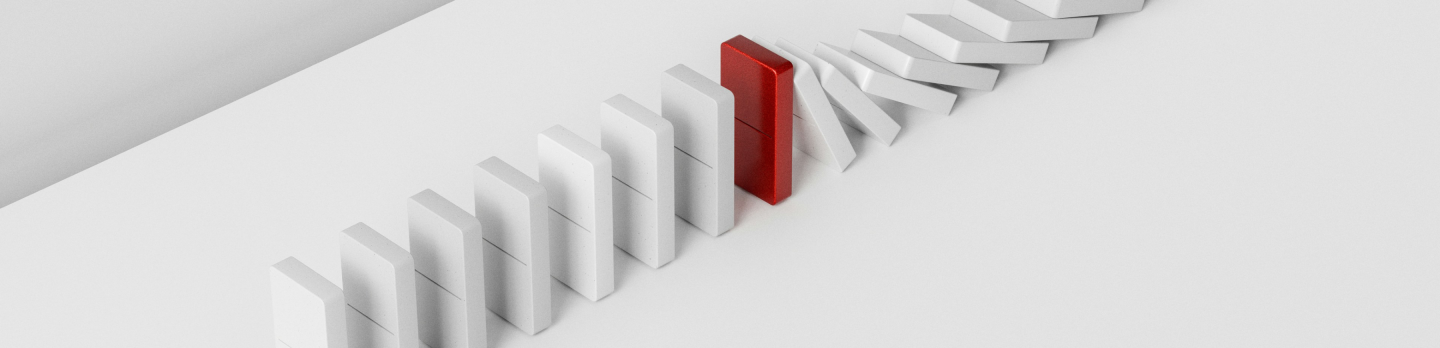 A line of white dominoes is arranged on a white surface, with one red domino standing upright, halting the others from falling, conveying interruption.