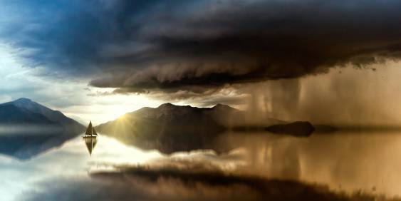 Boat at sea, moody sky. Mountains in the background. 