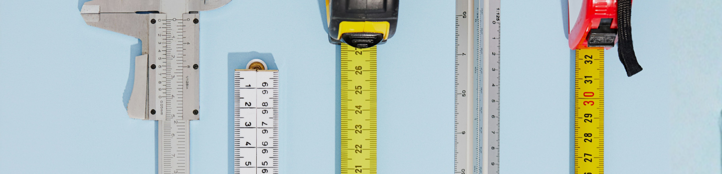 Measuring tools arranged on a light blue background: calipers, rulers, and yellow tape measures, conveying precision and accuracy.