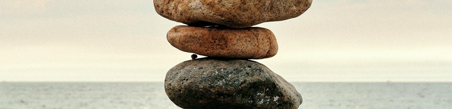A balanced stack of smooth rocks on a sandy beach, with gentle waves lapping in the background.