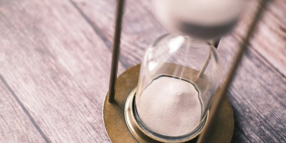 An hourglass filled with sand sits on a wooden table, casting a soft shadow in the ambient light.