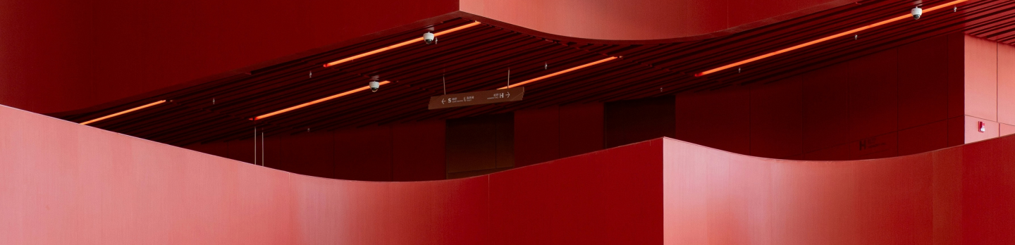 A minimalist red architectural interior with tall coral walls beneath a dark slatted ceiling and tiny lights, creating a dramatic, moody atmosphere.