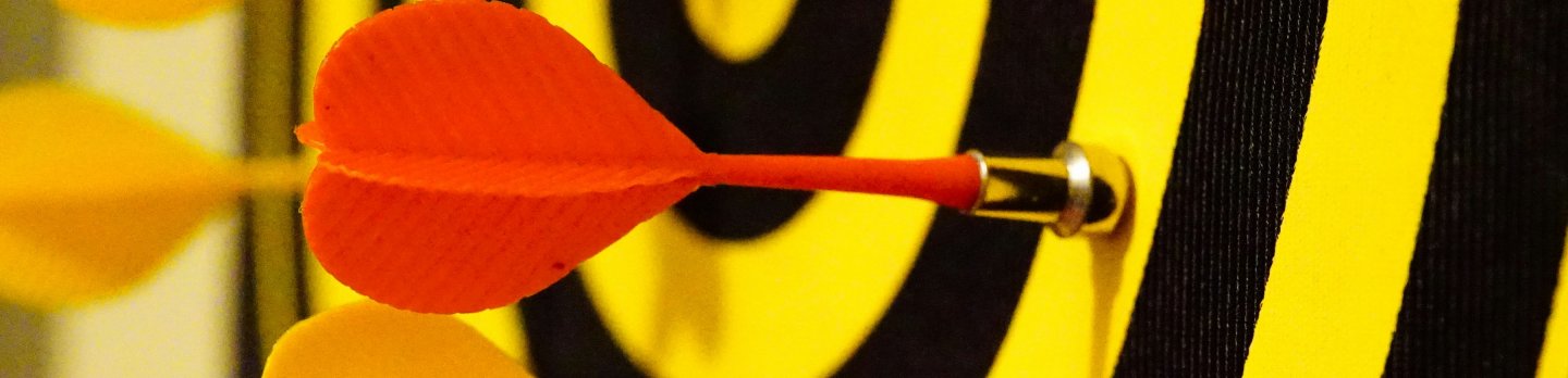 A red dart is precisely lodged in the bullseye of a yellow and black target, indicating focus.