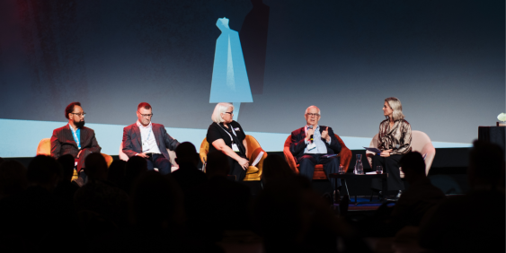  Panel of speakers sitting on stage at a conference, representing various backgrounds and expertise, discussing key topics.