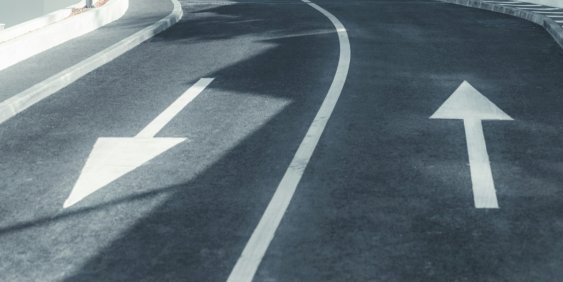 A road with two arrows indicating opposite directions, symbolizing diverging paths or choices ahead.