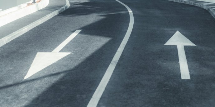 A road with two arrows indicating opposite directions, symbolizing diverging paths or choices ahead.
