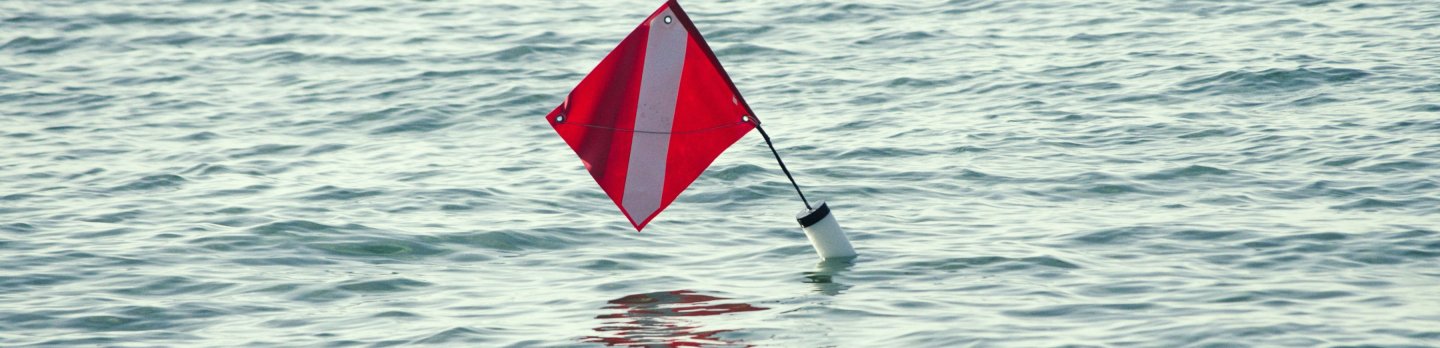 A red-and-white diamond-shaped nautical marker bobs on rippling blue-gray water, casting a faint reflection and creating a calm, solitary mood.