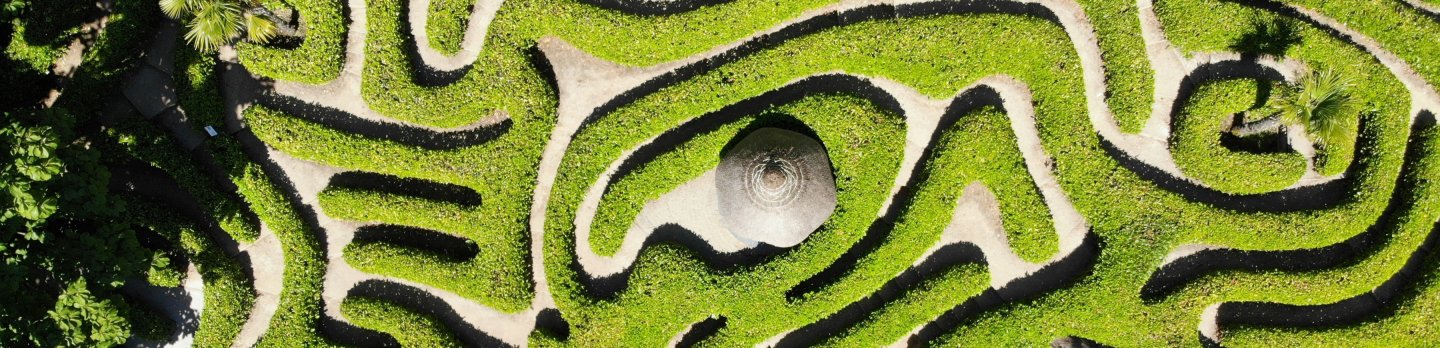 Aerial view of a complex maze situated in a green field, showcasing intricate pathways and surrounding landscape.