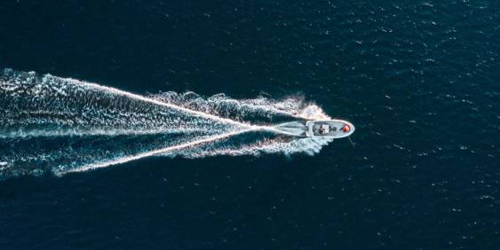 Overhead perspective of a boat moving across the vast ocean, leaving a wake in the water.