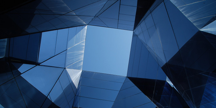 looking up through a blue black abstract glass building to the sky above 