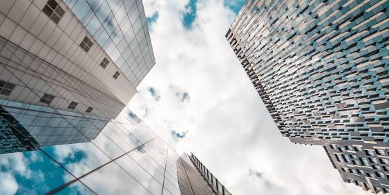 Looking up at three glass buildings and the sky beyond