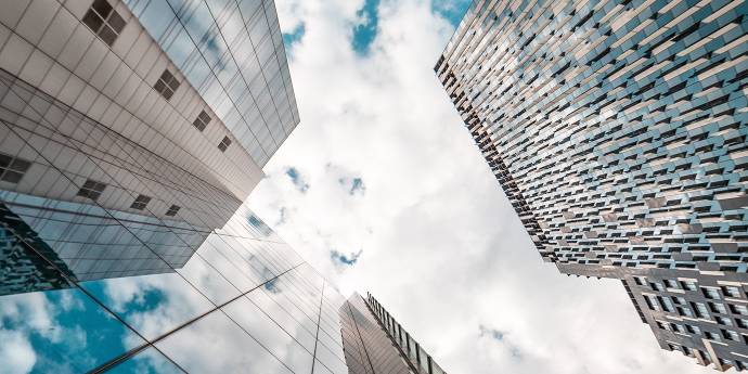 Looking up at three glass buildings and the sky beyond