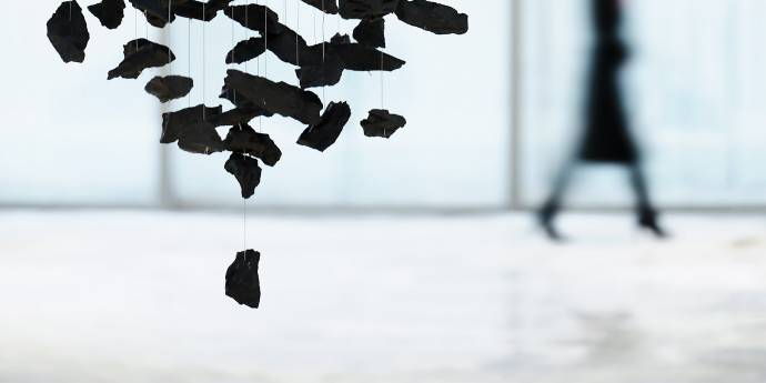 Broken black pieces hanging on a string with a woman walking in the background