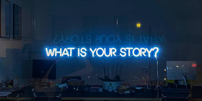 neon sign in window with words: What is your story?