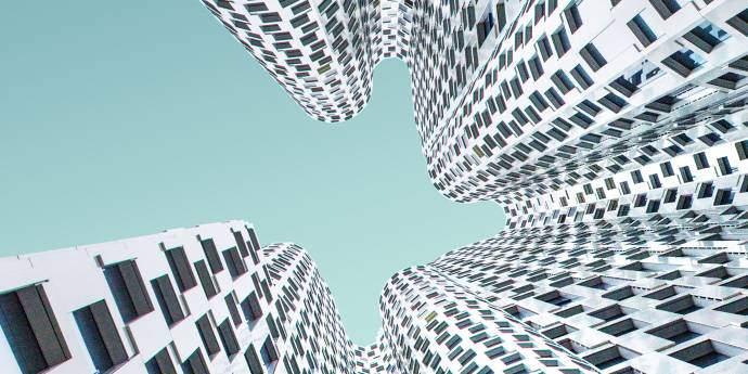 Looking up at a white and black hundertwasser-esque building to an aqua coloured sky