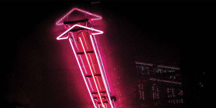 Pink neon arrow facing up on dark wall