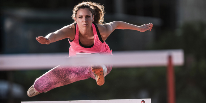 Female athlete jumping over hurdles 