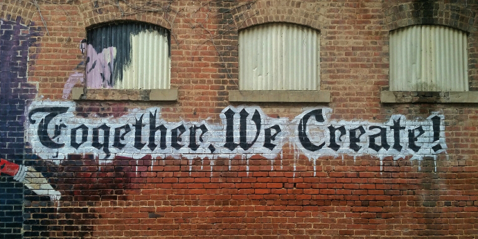 Brick wall with "together we will create "graffitied on it 