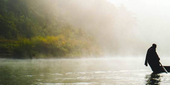 Mist over lake with man in fishing boat