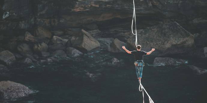 Man walking on tightrope across a cliff