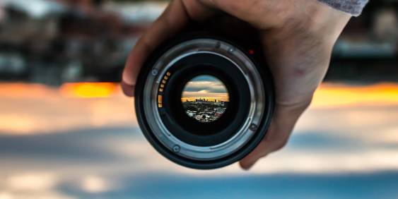 Man holding a camera lens with city scene in the distance