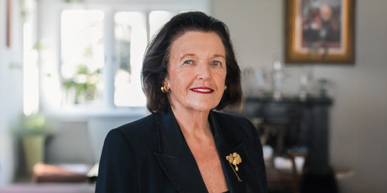 A woman in a tailored black suit with a gold pin.