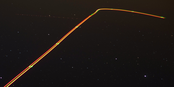 A series of glowing lights forms a long line in the sky, illuminating the darkness with their vibrant colors.